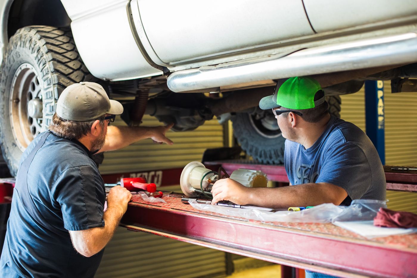 A mentor and student work together beneath a truck on a lift